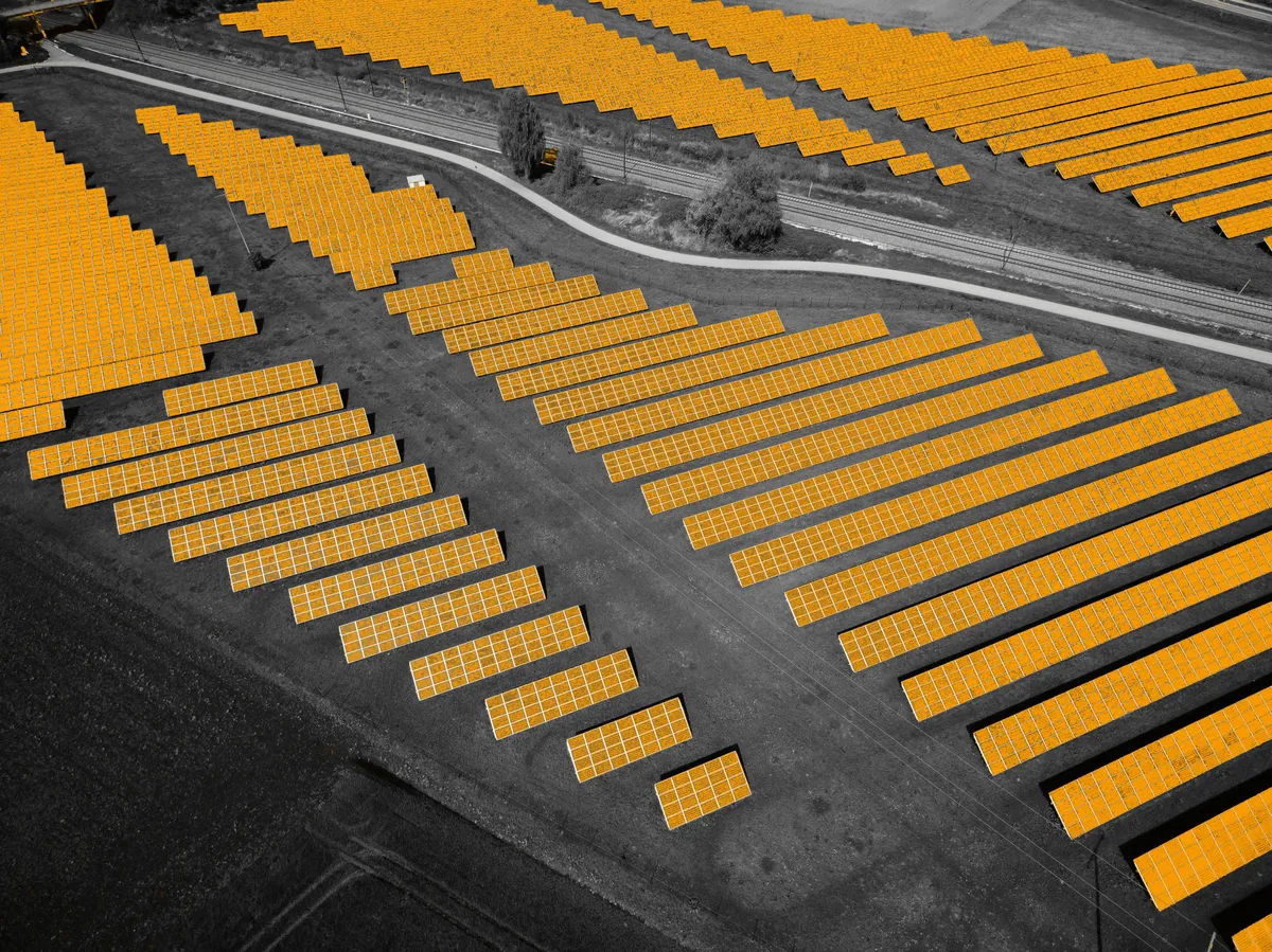 Aerial view of rows of solar panels, highlighted in orange, beside a railway line